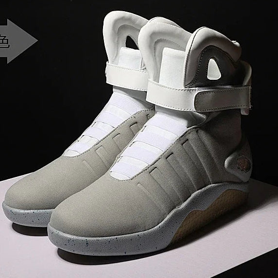 A pair of futuristic high-top sneakers shown in two views: one from the front on a white platform and one from the side showing the sole. The shoes feature a light gray and white upper with a tan sole, set against a black background.
