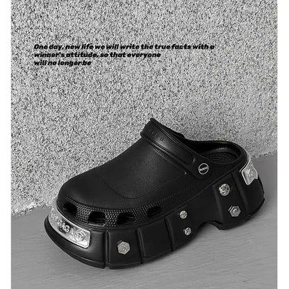 A black chunky clog-style shoe with metallic silver hexagon accents and a textured sole, photographed against a gray concrete-textured wall and floor. Black text is printed on the wall to the left.