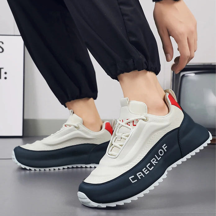 White and navy sneakers with red accents worn by a person, on a neutral background.